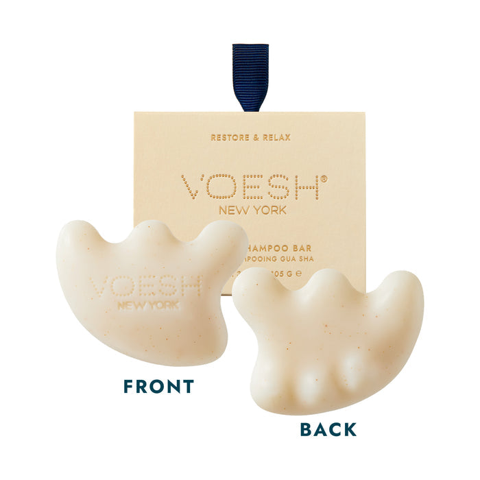 Image of a Voesh New York Restore & Relax shampoo bar in front of its packaging. The shampoo bar is white with an irregular, ergonomic shape resembling a gua sha tool. The bar is shown from both front and back, with Voesh New York branding visible on the front side.
