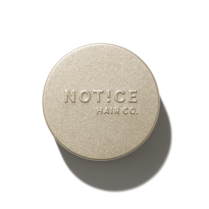 A round metallic Hair Bar Travel Tin by NOT!CE Hair Co., embossed with the brands name, is proudly plastic-free and recyclable. Its set against a white background with a shadow cast.