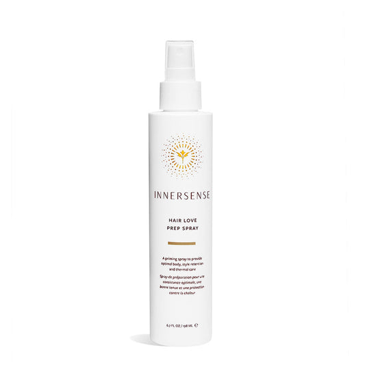 The Hair Love Prep Spray by Innersense Organic Beauty is in a white bottle with a spray nozzle, featuring a minimalist design. The packaging includes product information and a yellow sunburst logo above the brand name, enriched with organic aloe vera for nourishing care.