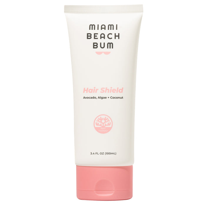 Miami Beach Bums Hair Shield is a reef-friendly leave-in conditioner in a white 3.4 FL OZ (100mL) tube, pink cap, featuring Avocado, Algae + Coconut on the label and a pink coral-like logo. It offers sun protection and is safe for color-treated hair.