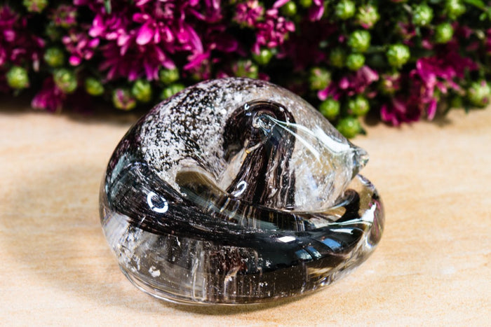 Grey cremains visible on the surface of a sleeping glass cat paperweight encased in clear glass.