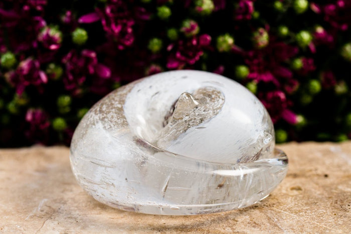 Clear glass sleeping cat paperweight with cremains visible inside, resting on a light surface.