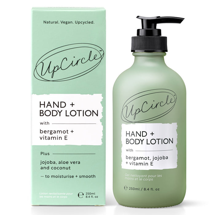 A green bottle of UpCircles Hand + Body Lotion with Bergamot Water, citrus-scented and enriched with vitamin E, sits beside its matching box. Featuring a black pump, it emphasizes natural vegan skincare with upcycled ingredients and text in English and French.