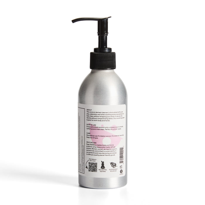 The sleek aluminum bottle of Soap Distillerys Hand + Body Wash features a black reusable pump and label with clear text and symbols, set against a plain white background.