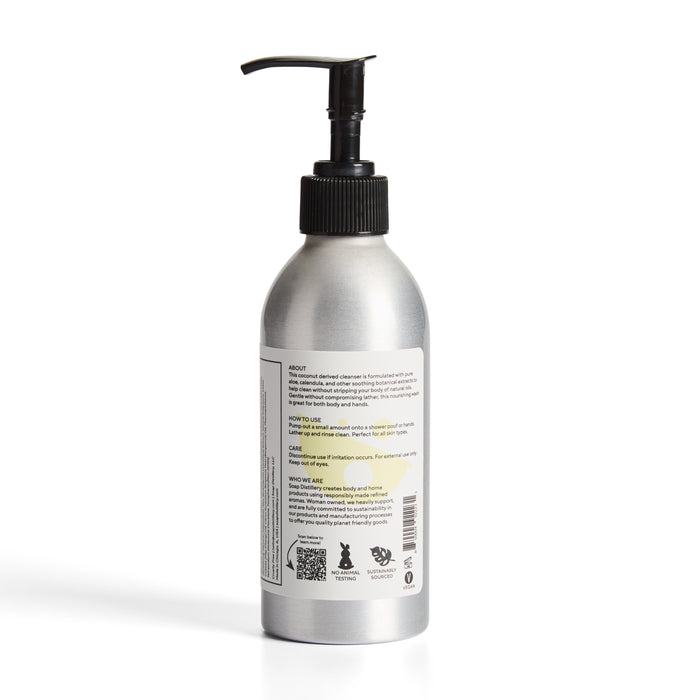 A silver aluminum Soap Distillery Hand + Body Wash bottle with a black pump and white label showing usage directions, recycling symbols, product info, and clear instructions on the back—perfect for hand or body cleansing.