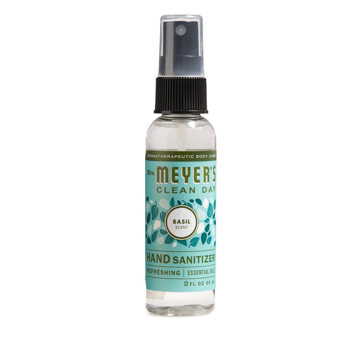 A 2 fl oz Mrs. Meyers Hand Sanitizer features a basil scent and 62% ethyl alcohol. The translucent spray bottle has a green label with plant illustrations, emphasizing its refreshing essential oil formula.