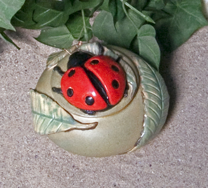 Red ladybug ceramic keepsake urn perched on a white flower with a yellow center viewed from above
