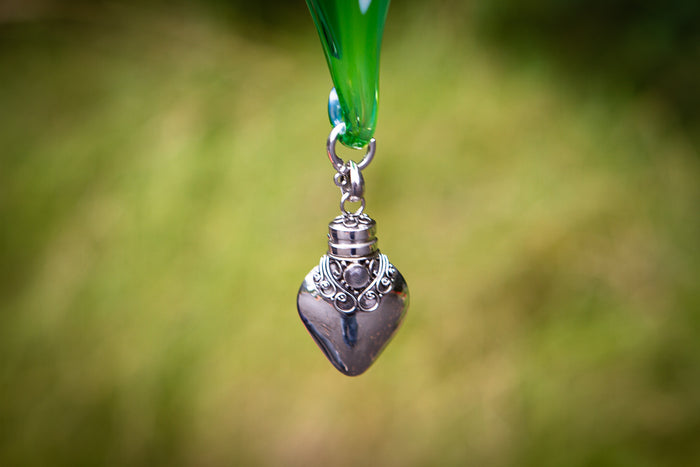 Green spotted glass teardrop ornament hanging from a ring with a silver ornate keepsake urn pendant