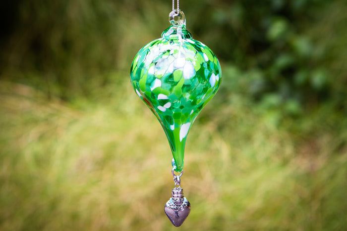 Green spotted teardrop glass ornament hanging from a silver chain with a decorative silver heart pendant at the bottom.