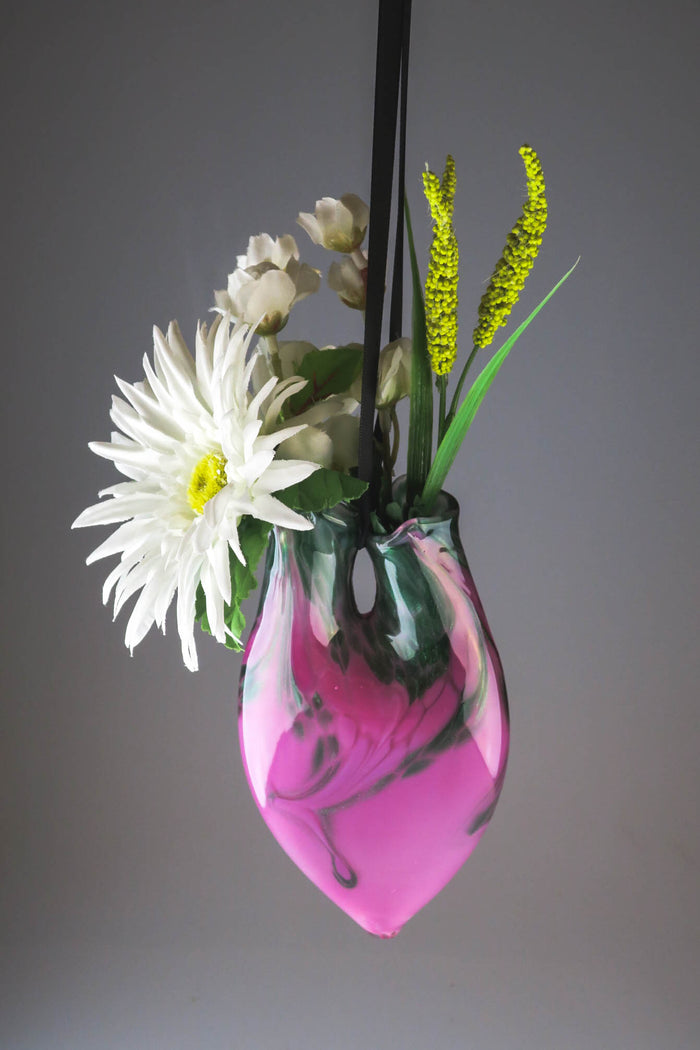 Hanging dual neck glass vase with pink and green marble finish holding flowers and cremains.