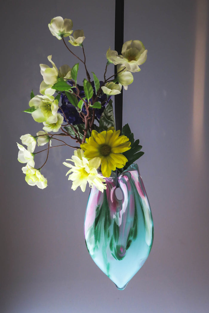 Hanging cremains vase in teal and pink marble with pale white blossoms.