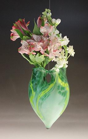 Hanging cremains vase in green marbled glass with pink and white flowers against a dark background.