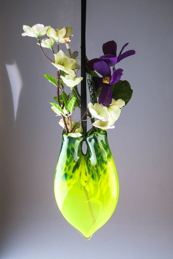 Lime green dual neck hanging glass vase with white blossoms and a purple bloom on stems.