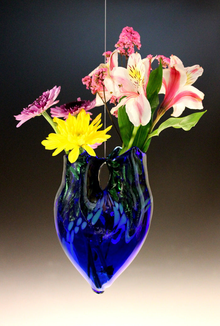 Cobalt blue hanging glass vase with a bouquet of pink blooms and white lilies.