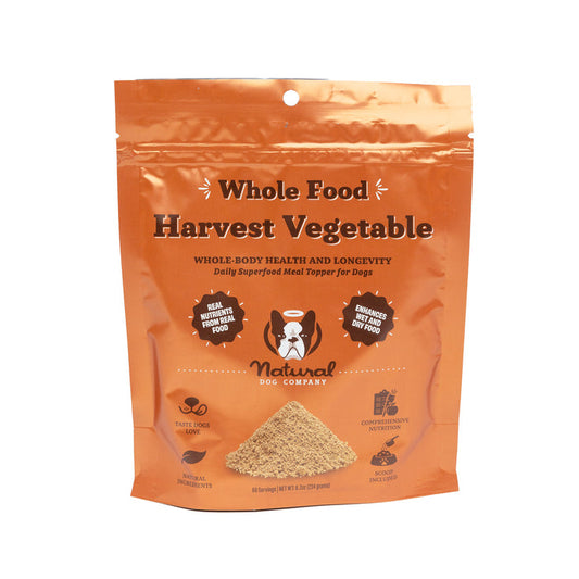 The orange packaging of Natural Dog Companys Harvest Vegetable Superfood Granules showcases its meal topper benefits, with text highlighting nutritional advantages and icons for taste, quality confidence, and digestive health. It also features an image of a dog and playful paw prints.