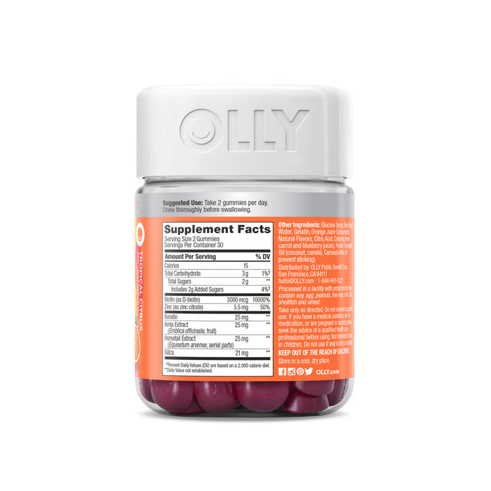 The OLLY Heavenly Hair bottle features a white lid and holds purple gummies with biotin. The label lists supplement facts and ingredients, advises taking two gummies daily, and prominently displays the brand name on the front.