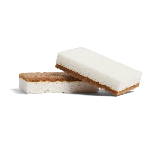 Two Grove Co. Heavy Duty Agave Scrubber Sponges, each with a white soft top and brown abrasive bottom, are shown—one lying flat and the other propped diagonally—against a white background.