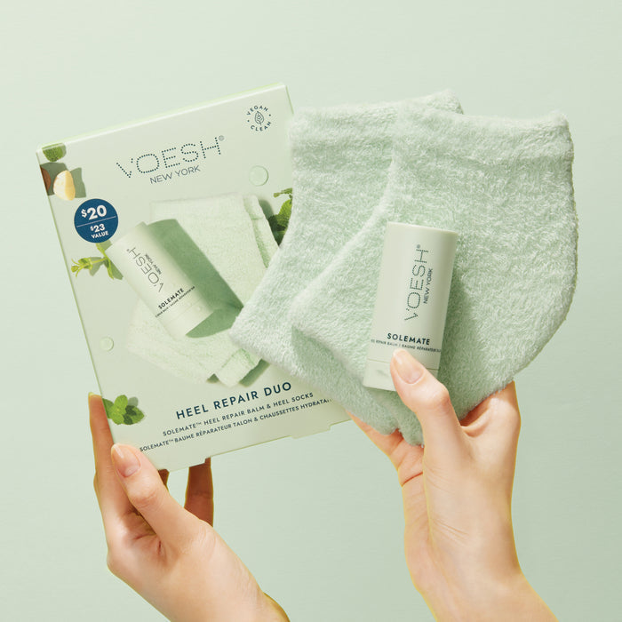 Hands holding VOESH New Yorks Heel Repair Duo—with Solemate Heel Repair Balm and Moisturizing Heel Socks—against a light green background. Price: $20.