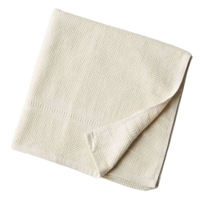 The Anact Hemp and Organic Cotton Bath Towel is cream-colored with a textured pattern and border design. Neatly folded, one corner turns up slightly, revealing its soft thickness.