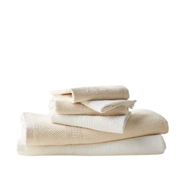 A stack of neatly folded cream-colored towels from Anact’s Hemp and Organic Cotton Bath Towel Set sits against a plain white background, with smaller ones on top and larger ones at the bottom.
