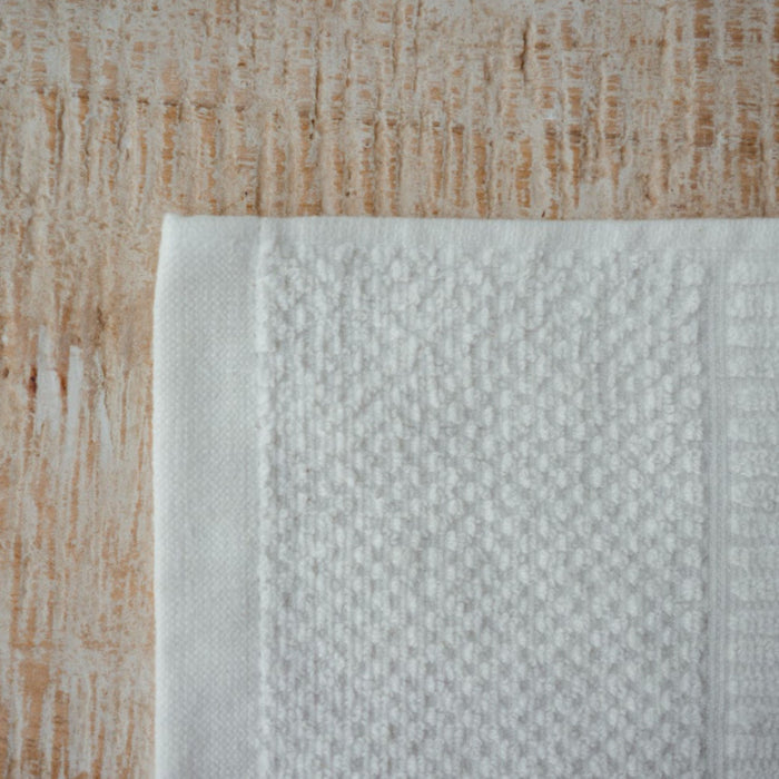 A close-up features an Anact Hemp and Organic Cotton Hand Towel on a wooden surface. The folded towel displays a dense weave against the light wood grain, highlighting its dye-free, textured design. Crafted from organic cotton, it is gentle on skin and eco-friendly.