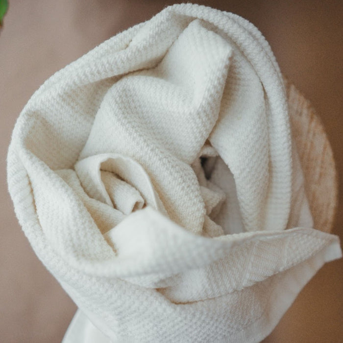 A close-up of the Hemp and Organic Cotton Hand Towel by Anact showcases its beige, textured fabric folded like a rose. The dye-free towels woven pattern and soft appearance form an artistic, floral shape against a neutral background.