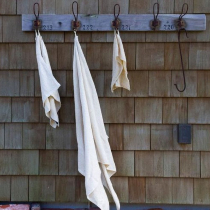 Hooks labeled 223, 222, 221, and 220 are mounted on a wooden shingled wall. Anact Hemp and Organic Cotton Hand Towels hang on three hooks, while the fourth holds a large metal hook.