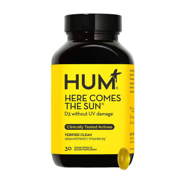 A bottle of HUM Nutritions Here Comes The Sun Vitamin D3 Supplement features a yellow and black label with D3 without UV damage and Clinically Tested Actives claims to boost mood. A single capsule is depicted next to the bottle.