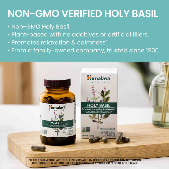 A bottle and box of Himalaya Holy Basil Supplement Capsules on a wooden table. The bottle is open with capsules spilling out. The text on the image highlights the product's features including non-GMO, plant-based, promotes relaxation, and being family-owned since 1930.