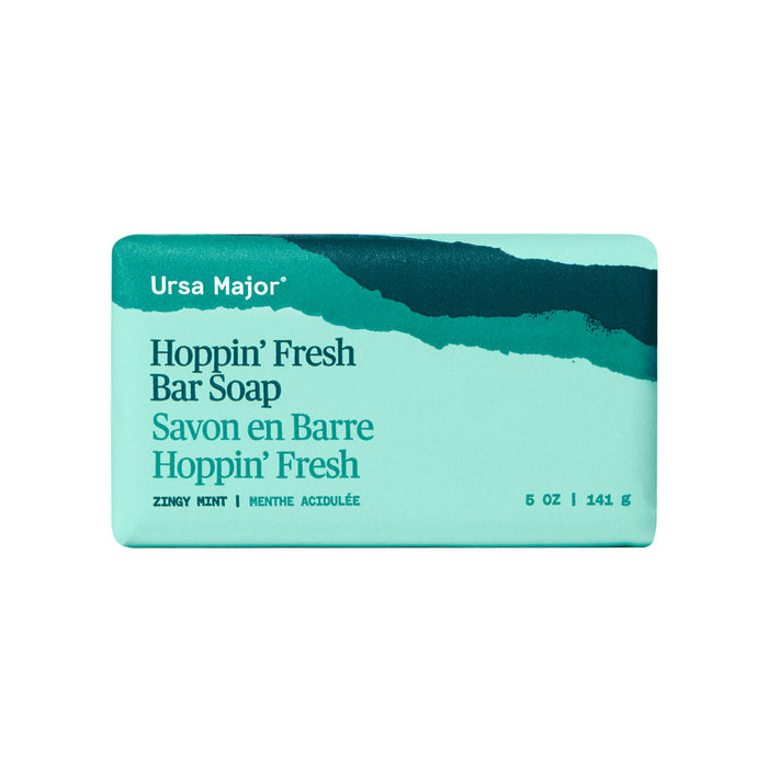 A turquoise bar of Ursa Major Morning Mojo Bar Soap in its packaging, with white and dark teal text and a wavy dark teal design on top. Made with natural products, this zesty mint exfoliating soap comes in a 5 oz size.