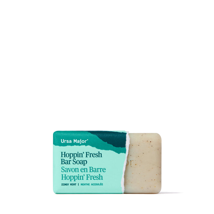 A rectangular bar of Ursa Major Morning Mojo Bar Soap, made with natural exfoliants, is partially wrapped in a teal and white label featuring product details in English and French, displayed on a white background.