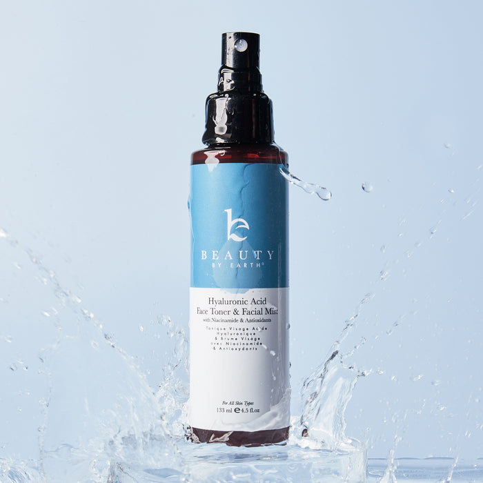 A Beauty by Earth Hyaluronic Acid Toner bottle is set against a light blue backdrop. Water splashes around the dark bottle, enhancing its refreshing and moisturizing effects for youthful skin.