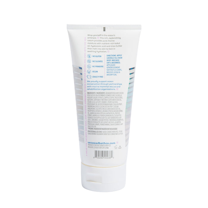 A white tube of The Seaweed Bath Co Hydrating Body Cream features blue accents. The back label emphasizes product details, vegan and cruelty-free attributes in organic skin care. It has a white cap and stands upright.