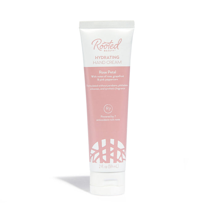 Rooted Beauty Hydrating Hand Cream in Rose Petal scent, packed with plant-based moisturizers and shea butter, comes in white and pink packaging highlighting pink grapefruit and pink peppercorn. Perfect for dry skin, this 2 fl oz (59 mL) cream offers lush hydration.