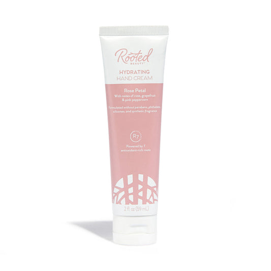 Rooted Beauty Hydrating Hand Cream in Rose Petal scent, packed with plant-based moisturizers and shea butter, comes in white and pink packaging highlighting pink grapefruit and pink peppercorn. Perfect for dry skin, this 2 fl oz (59 mL) cream offers lush hydration.
