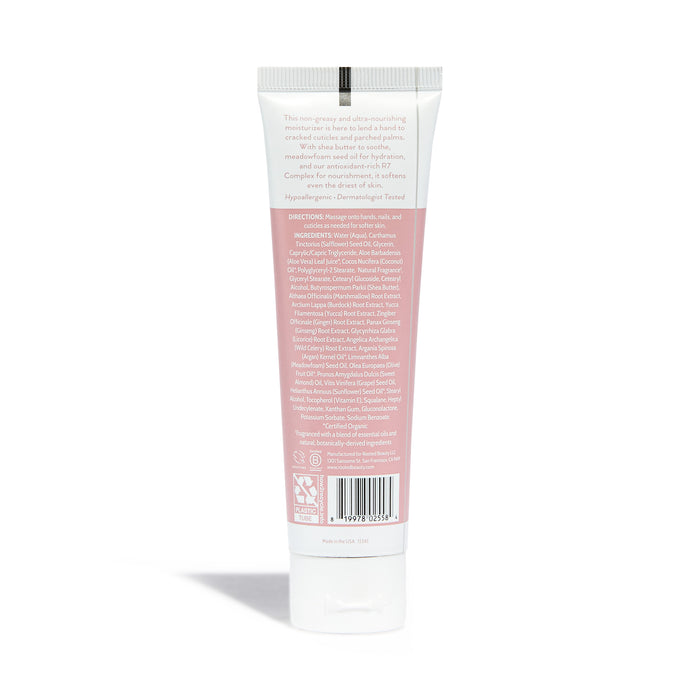 A tube of Rooted Beauty Hydrating Hand Cream with a pink label on the back lists plant-based moisturizers, ingredients, and directions. It has a white cap, and the text about soothing dry skin is in small, white font.