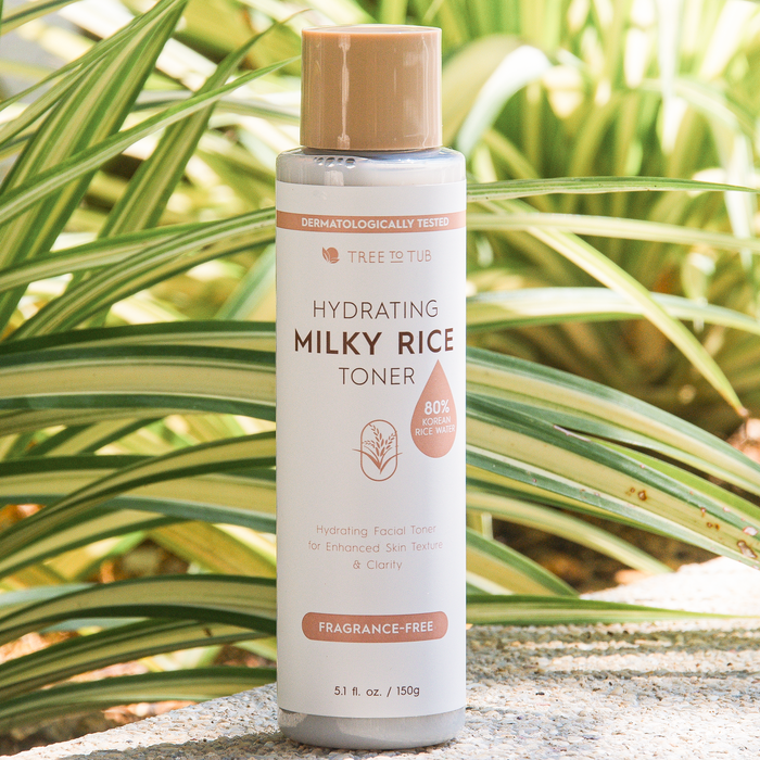 Tree To Tubs Hydrating Milky Rice Toner for Dry & Dehydrated Skin sits outdoors in lush greenery, showcasing its fragrance-free label and 80% rice water content, designed to enhance skin texture and clarity.