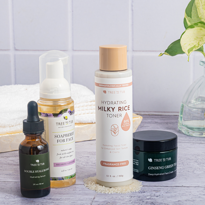 Tree To Tubs Hydrating Milky Rice Toner for Dry & Dehydrated Skin adorns the bathroom countertop alongside a face wash, serum, and cream. A stack of towels and a green plant complete the elegant scene.