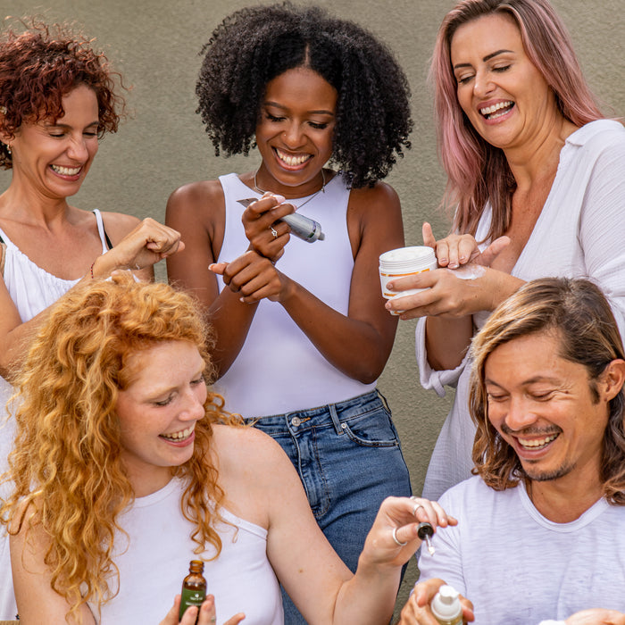 Five people joyfully apply Tree To Tubs Hydrating Milky Rice Toner for Dry & Dehydrated Skin outdoors, holding various containers. Wearing casual white tops, they engage in their skincare ritual against a minimalist neutral gray wall, adding vibrancy to the shared experience.