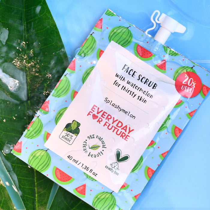 A pouch of Hydrating Watermelon Face Scrub by Everyday For Future sits on a blue surface with a large green leaf. This vegan product boasts 98% natural origin and cruelty-free claims, being 98% plastic-free and 20% used.