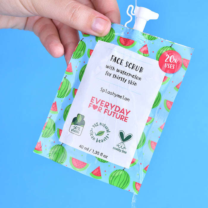 A hand holds a colorful Everyday For Future pouch labeled Hydrating Watermelon Face Scrub for thirsty skin. The packaging features watermelon illustrations and eco-friendly icons, stating 20% plastic, 99% natural clean beauty, vegan, and cruelty-free.