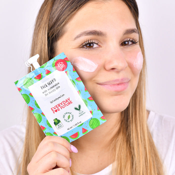 A person smiles with two patches of face scrub on their cheeks, holding a colorful pouch labeled Everyday For Future. Featuring vibrant watermelon designs, the Hydrating Watermelon Face Scrub is vegan and contains natural ingredients like almond oil for healthy skin.