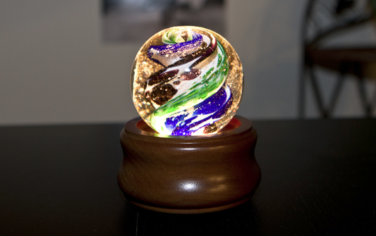 Brown wooden illuminated stand displaying a colorful glass orb to showcase Spirit Pieces
