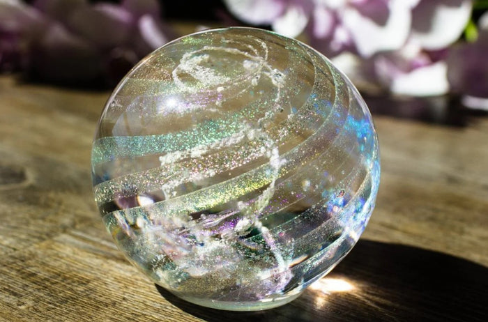 Dichroic rainbow glass orb holding cremains on a wooden surface.