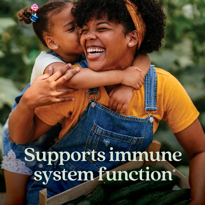A smiling woman in overalls holds a basket of cucumbers as a young girl hugs and kisses her cheek. The text reads, New Chapter Immune Defense Vitamin C+ Gummies, Citrus Flavored—supports immune system function* with Acerola Cherry.