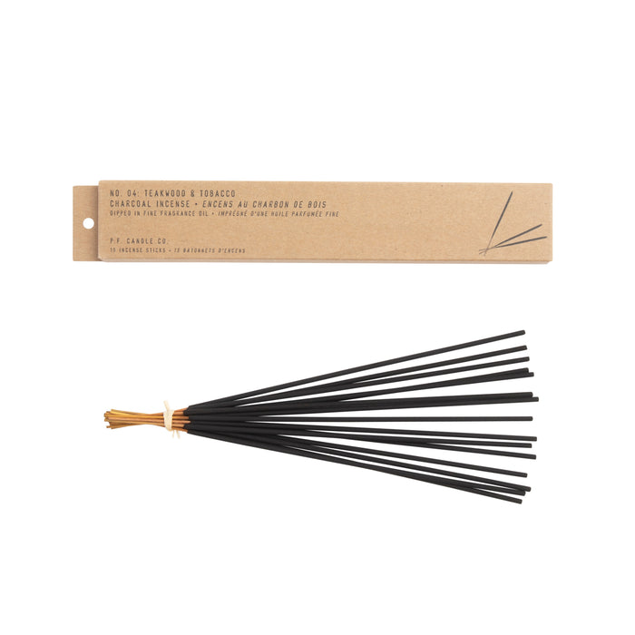A bundle of P.F. Candle Co.s black charcoal incense sticks, scented with Teakwood & Tobacco, is tied with a tan string beneath a labeled brown box highlighting its exceptional characteristics.