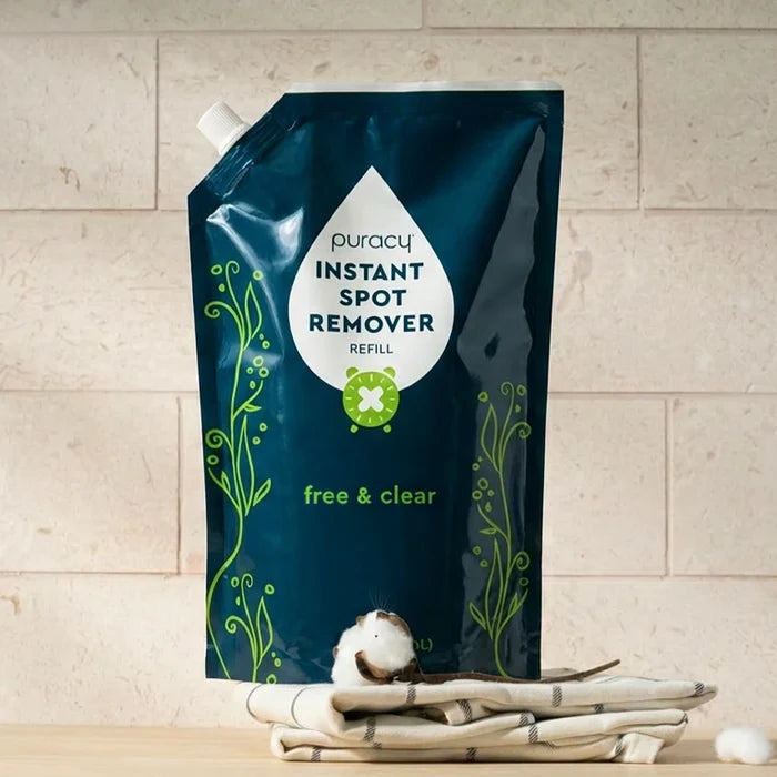 Dark green refill pouch of Instant Spot Remover on folded towels with a cotton ball.