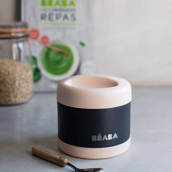 A sleek BEABA Insulated Stainless Steel, Kid Friendly Food Container Jar with a black and pink design sits on the countertop. In the background, theres a grain container and green puree package. A spoon rests beside this leakproof jar, ensuring temperature-controlled meal enjoyment.