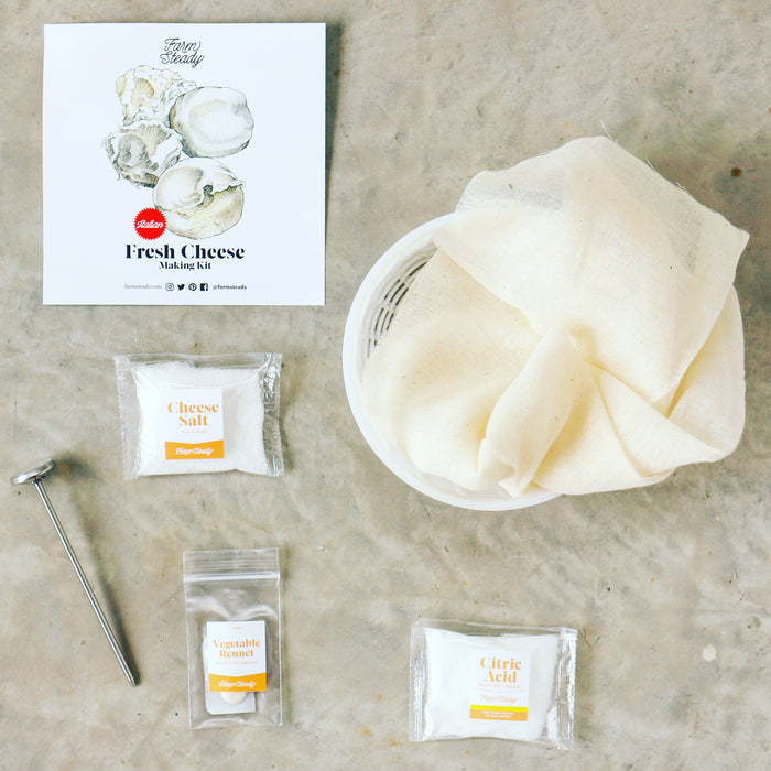 The FarmSteady Italian Fresh Cheese Making Kit on a gray surface includes essentials like a mesh cloth, strainer, and thermometer. Craft ricotta or mozzarella with packets labeled Cheese Salt, Vegetable Rennet, and Citric Acid, plus an instruction booklet featuring a cheese illustration.