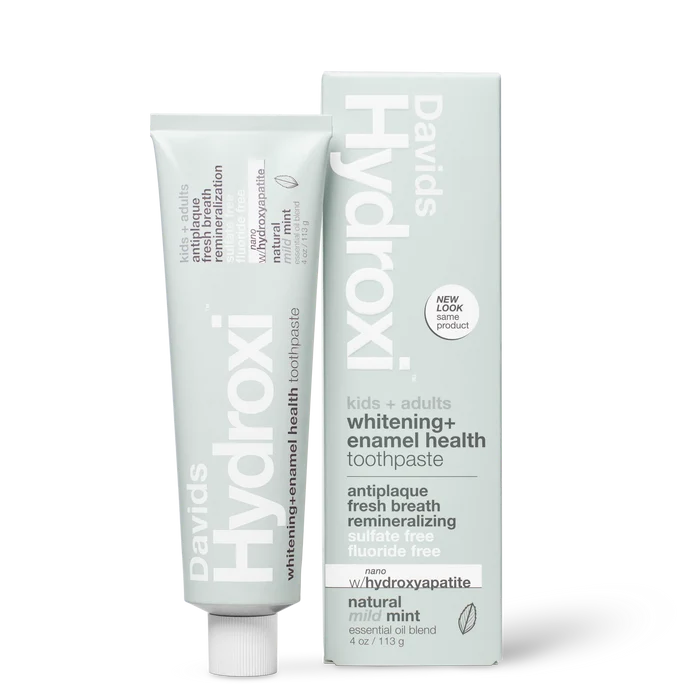 A tube and upright box of Davids Hydroxi Whitening + Enamel Health Toothpaste w/nano hydroxyapatite, labeled for natural whitening and enamel health for kids and adults. This fluoride-free toothpaste offers a mild mint flavor and the benefits of nano hydroxyapatite. The box stands upright beside the tube.